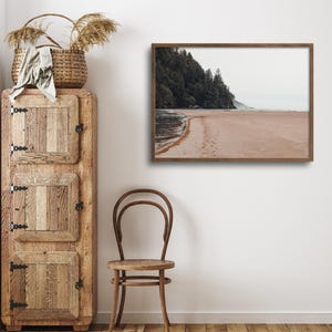 Peut inclure: Une photographie encadr&eacute;e d'une sc&egrave;ne de plage avec un rivage sablonneux, une ligne d'arbres et un ciel nuageux. La photographie est dans un cadre en bois brun et est accroch&eacute;e &agrave; un mur blanc.