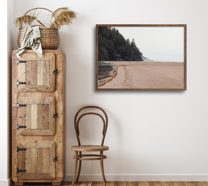 Peut inclure: Une photographie encadr&eacute;e d'une sc&egrave;ne de plage avec un rivage sablonneux, une ligne d'arbres et un ciel nuageux. La photographie est dans un cadre en bois brun et est accroch&eacute;e &agrave; un mur blanc.
