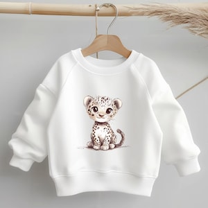 Könnte beinhalten: Weißer Pullover mit einem niedlichen Cartoon-Leoparden-Druck. Der Leopard sitzt und hat ein braunes und schwarzes geflecktes Muster.