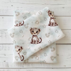 Könnte beinhalten: Ein weißer Stoff mit einem hellblauen Muster aus Leopard-Jungen und Pfotenabdrücken. Der Stoff ist in der Mitte gefaltet und das Muster ist auf beiden Seiten sichtbar.
