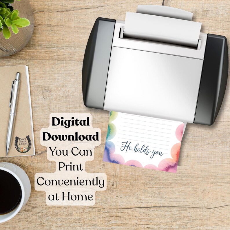 May include: A printer is shown printing a colorful card with the text "He holds you." The card has a watercolor design with pink, blue, and green hues. The image also includes text that reads "Digital Download You Can Print Conveniently at Home."