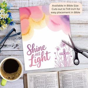 May include: A print with watercolor clouds in pink, yellow, and purple hues. The text "Shine His Light" is in a script font. A cross and floral design are on the right. The print is available in Bible size, cutting out to 7x9 inches.