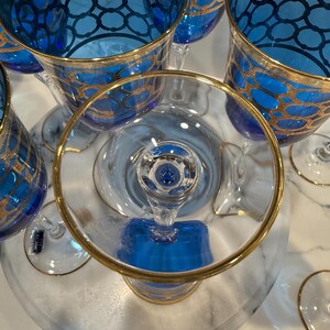 May include: A collection of elegant blue and gold-rimmed glassware. The glasses feature a detailed gold geometric pattern on the blue bowls. The stems and bases are clear, creating a sophisticated aesthetic. Ideal for special occasions.