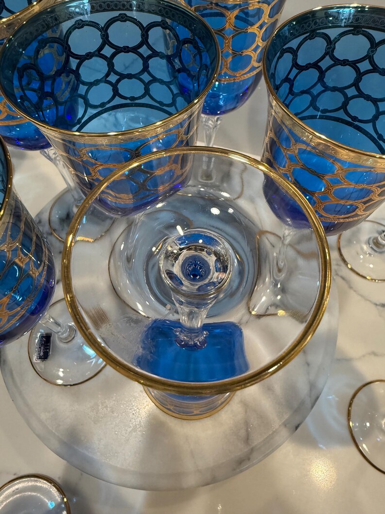 May include: A collection of elegant blue and gold-rimmed glassware. The glasses feature a detailed gold geometric pattern on the blue bowls. The stems and bases are clear, creating a sophisticated aesthetic. Ideal for special occasions.