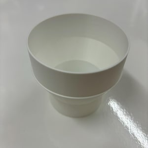 May include: A white plastic container with a cylindrical top and a slightly smaller base. The container has a smooth, clean surface and appears to be empty. The design is simple and functional.