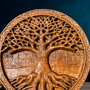 May include: A circular wooden wall hanging featuring an intricately carved tree of life. The tree has detailed branches and roots, and the carving is surrounded by a Celtic knot border.