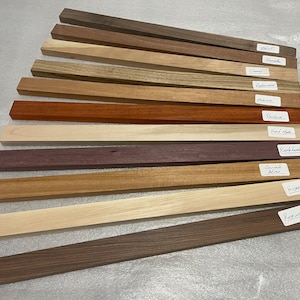 May include: A collection of 10 different wood samples, each labeled with its name. The samples are arranged in a fan shape, with the labels facing the viewer. The wood types are: Walnut, Sapele, Cherry, Zebrawood, Cocobolo, Padauk, Hard Maple, Purpleheart,  Genuine  Alas, Hickory, and Rosewood.