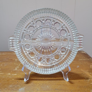 Op de afbeelding: Een glazen serveerschaal met een decoratief stervormig patroon. De schaal staat op een transparante kunststof standaard.