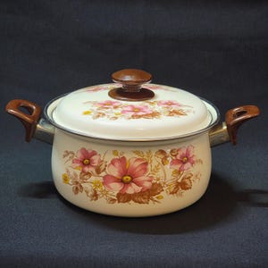 May include: White enamel pot with a floral design in shades of pink and brown. The pot has a wooden knob on the lid and two brown handles.