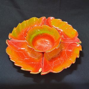 Op de afbeelding: Een serviesset van keramiek met vier blaadjesvormige kommen en een centrale kom. De kommen zijn oranje, geel en groen met gouden randjes.