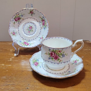 Puede incluir: Una taza de té y un platillo blancos con un patrón floral. La taza tiene un borde dorado y el platillo tiene un borde festoneado.