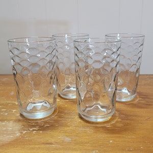 May include: Four clear glass tumblers with a textured, bubbled design. The glasses are empty and sitting on a wooden surface.
