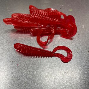 May include: A pile of red plastic fishing lures with a ribbed texture and a glitter finish.