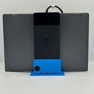 May include: A black Dell laptop with a black charging block and a blue stand. The laptop is open, displaying the screen. The stand is holding the charging block in place.