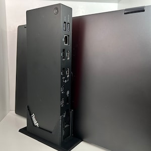 May include: A black laptop stand with a ThinkPad logo and multiple ports on the side. The stand is holding a black laptop.