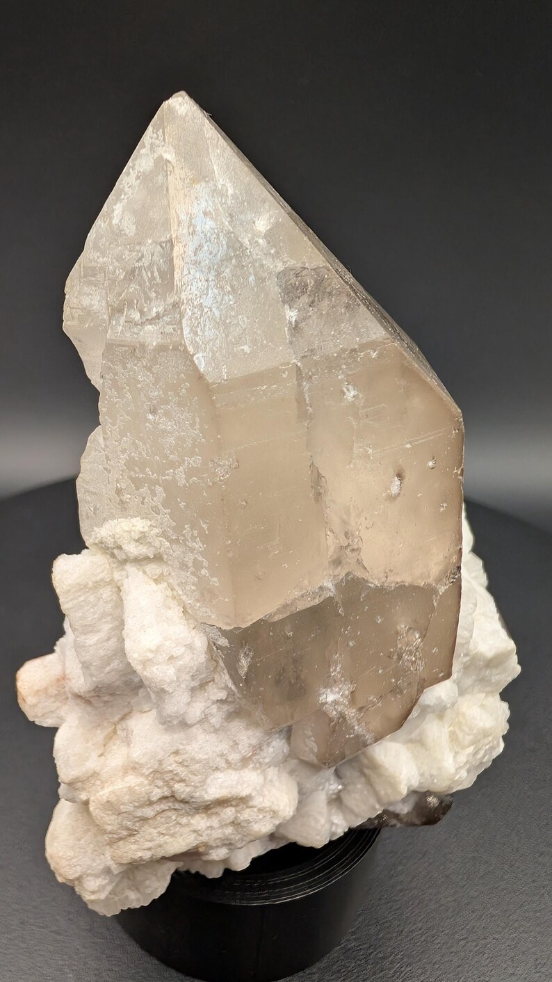 May include: A large, clear quartz crystal with a smoky brown hue, resting on a bed of white, crystallized matrix. The crystal is faceted and has a sharp point.