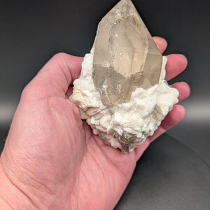 May include: A large, clear quartz crystal with a smoky brown hue, resting on a bed of white calcite crystals.