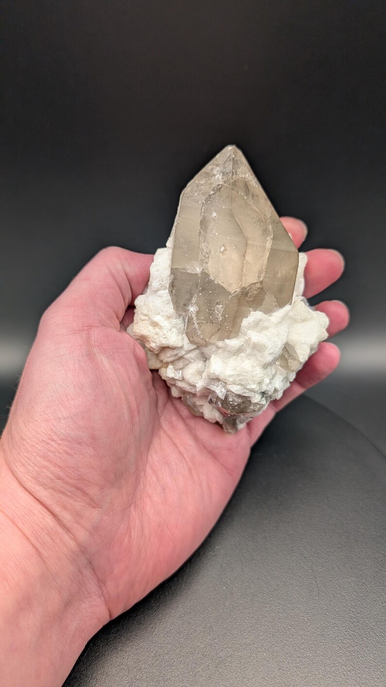May include: A large, clear quartz crystal with a smoky brown hue, resting on a bed of white calcite crystals.