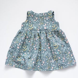 May include: A sleeveless, light blue dress with a floral print. The dress has a gathered skirt and a simple, round neckline.