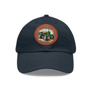 Op de afbeelding: Marineblauwe baseballcap met een ronde patch met een vintage groene tractor. De patch bevat de tekst "Spring Bluff Est. 1872". De cap heeft een gebogen klep en een klassiek zes-panelen ontwerp.