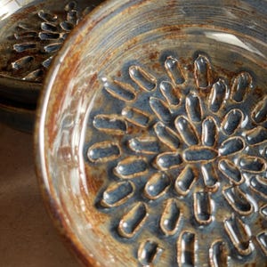 Puede incluir: Un cuenco de cerámica azul y marrón con un diseño texturizado en relieve. El cuenco tiene un aspecto rústico y hecho a mano.