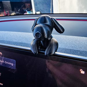 K&ouml;nnte beinhalten: Eine schwarze, 3D-gedruckte Hunde-Figur, die auf dem Armaturenbrett eines Autos sitzt. Der Hund hat gro&szlig;e, schlaffe Ohren und eine strukturierte Oberfl&auml;che. Das Armaturenbrett zeigt die Worte "Self-Driving".
