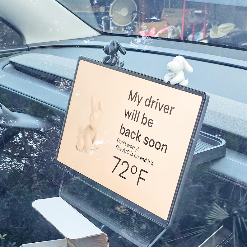 K&ouml;nnte beinhalten: Ein Autoschild mit dem Text "My driver will be back soon". Das Schild hat einen schwarzen Rahmen und ist mit kleinen Hundefiguren verziert. Die Temperatur wird mit 22&deg;C angezeigt.