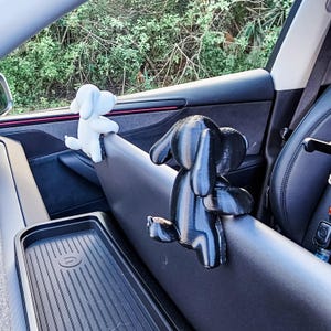 K&ouml;nnte beinhalten: Zwei hundeartige Autozubeh&ouml;rteile, eines wei&szlig; und eines schwarz, sind im Innenraum des Autos befestigt. Der wei&szlig;e Hund befindet sich links und der schwarze Hund rechts. Das Zubeh&ouml;r scheint aus Kunststoff oder einem &auml;hnlichen Material zu bestehen.