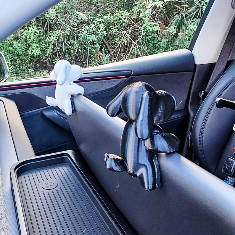 K&ouml;nnte beinhalten: Zwei hundeartige Autozubeh&ouml;rteile, eines wei&szlig; und eines schwarz, sind im Innenraum des Autos befestigt. Der wei&szlig;e Hund befindet sich links und der schwarze Hund rechts. Das Zubeh&ouml;r scheint aus Kunststoff oder einem &auml;hnlichen Material zu bestehen.