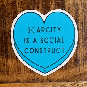 May include: A blue heart-shaped sticker with the text "SCARCITY IS A SOCIAL CONSTRUCT" in dark blue lettering.
