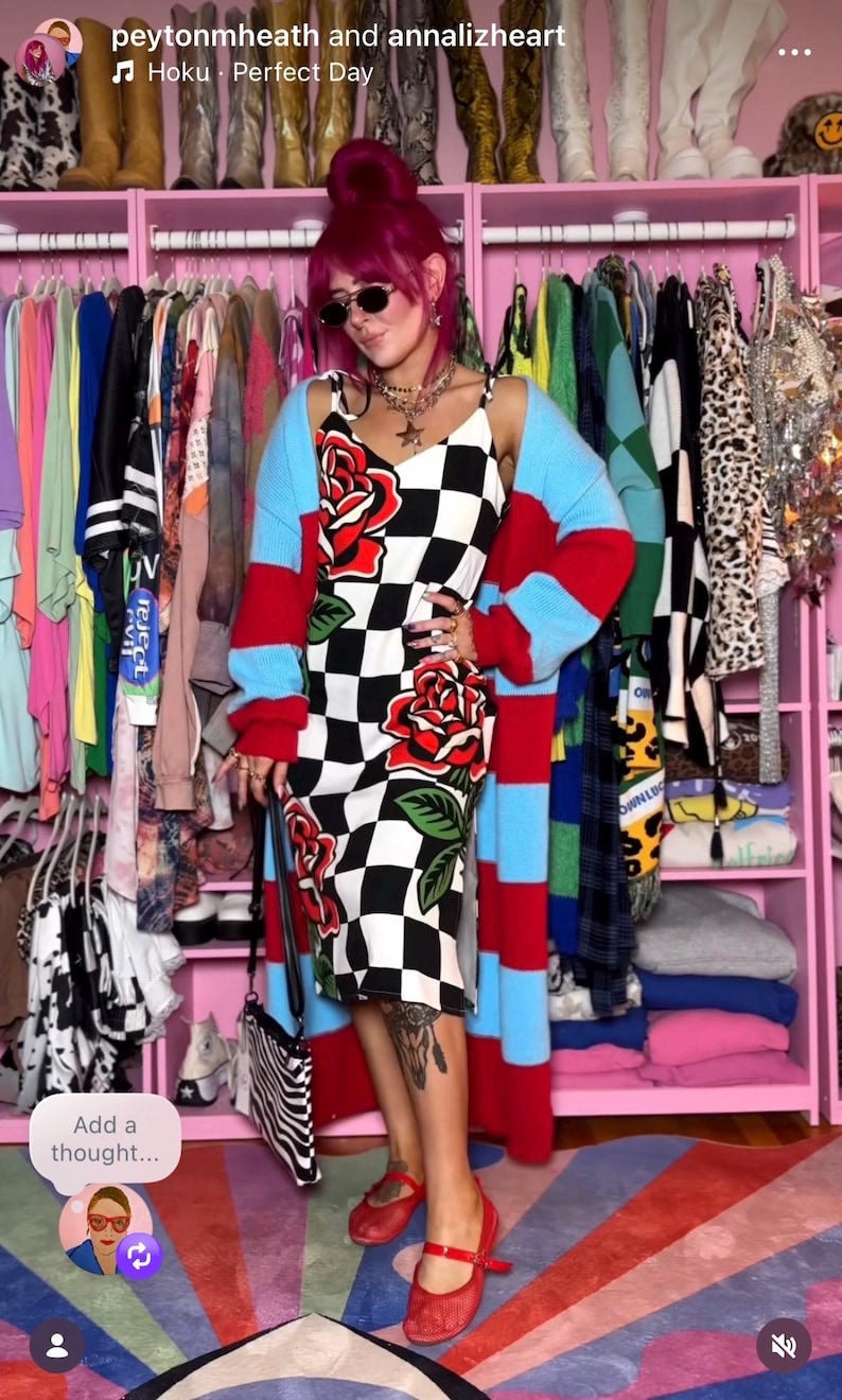 May include: A midi-length dress featuring a black and white checkered pattern with large red rose graphics, worn with a long-sleeved, open-front cardigan with horizontal red and light blue stripes, and a pair of red flat shoes with a strap.