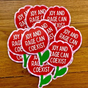 Peut inclure: Plusieurs autocollants rouges en forme de fleur avec l'inscription blanche "JOY AND RAGE CAN COEXIST". Les fleurs ont des tiges et des feuilles vertes, et une bordure rose et blanche &agrave; carreaux.