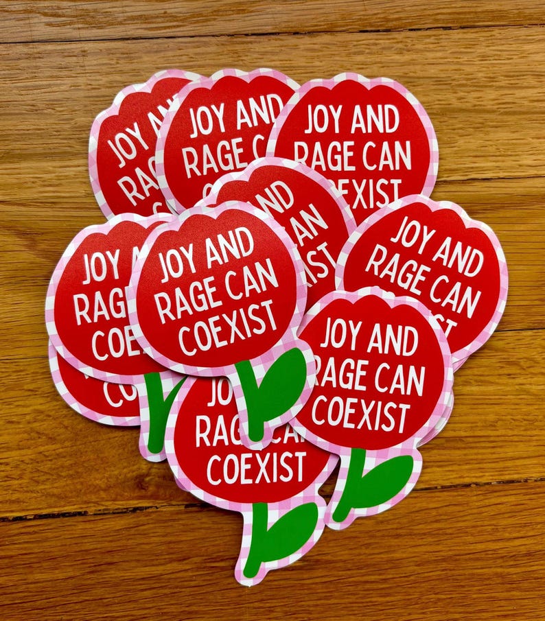 Peut inclure: Plusieurs autocollants rouges en forme de fleur avec l'inscription blanche "JOY AND RAGE CAN COEXIST". Les fleurs ont des tiges et des feuilles vertes, et une bordure rose et blanche &agrave; carreaux.