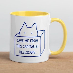 May include: White ceramic mug with a yellow rim and handle. The mug features a blue line drawing of a cat in a box with the text "Save me from this capitalist hellscape."