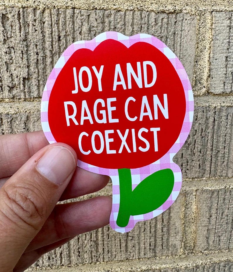 Peut inclure: Un autocollant en forme de fleur avec un centre rouge et une bordure rose et blanche &agrave; carreaux. L'autocollant porte les mots "JOY AND RAGE CAN COEXIST" en texte blanc. Une tige et une feuille vertes en bas.