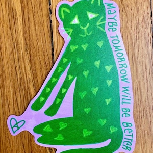 Op de afbeelding: Een groene sticker met een gestileerde luipaard met hartvormige vlekken. De luipaard is groen omlijnd en zit op een lavendelkleurige achtergrond. De tekst "MAYBE TOMORROW WILL BE BETTER" staat in het wit aan de rechterkant.