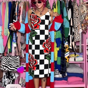 May include: A black and white checkered midi dress featuring large red rose graphics with green leaves, worn under a long, open-front cardigan with thick horizontal stripes in red and light blue. A black and white zebra-print handbag is held at the side.