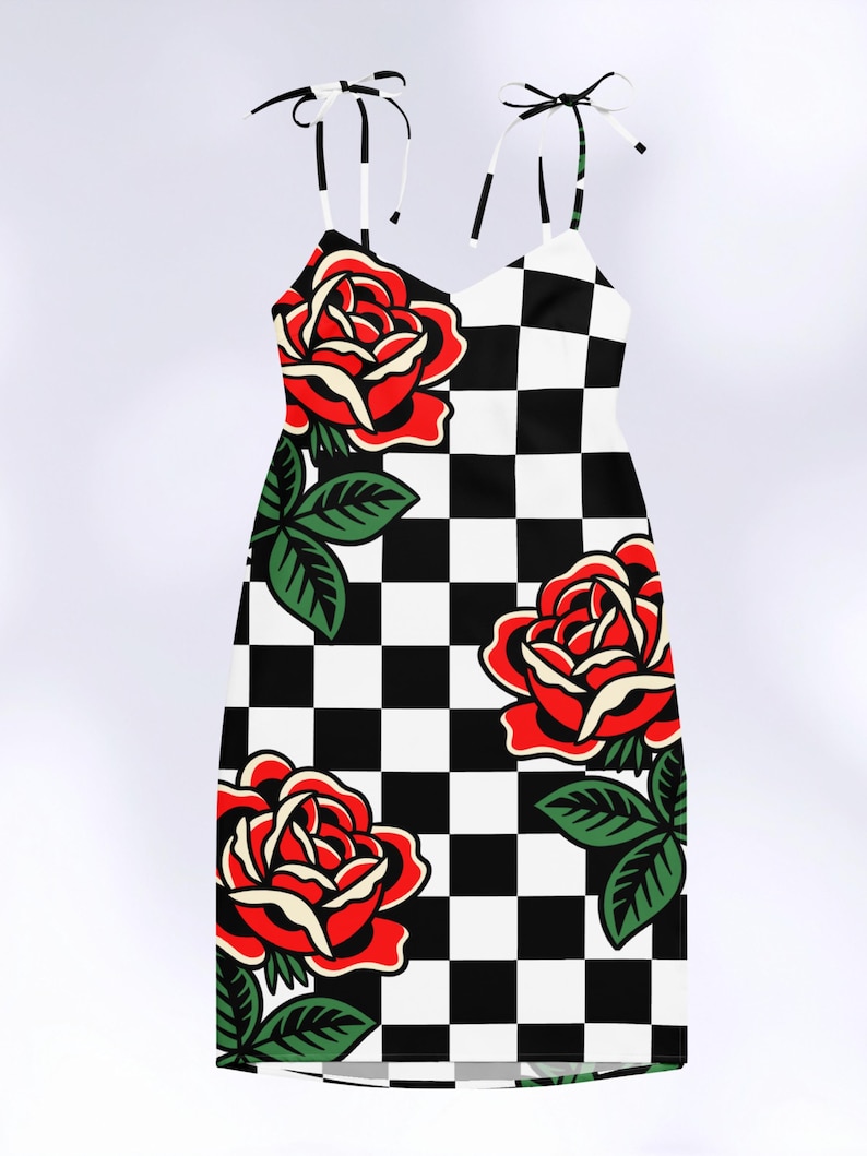 May include: A sleeveless dress featuring a black and white checkered pattern throughout. The garment is decorated with large, vibrant red roses with cream-colored highlights and green leaves. It includes thin, adjustable tie-up shoulder straps.