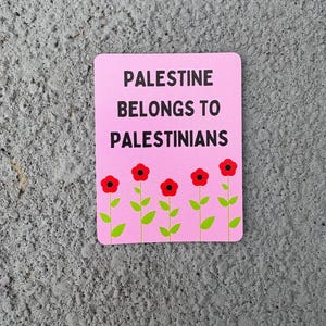 Może przedstawiać: R&oacute;żowy naklejka z tekstem "Palestine belongs to Palestinians" w czarnym kolorze. Pięć czerwonych kwiat&oacute;w z zielonymi łodygami i liśćmi znajduje się na dole naklejki.