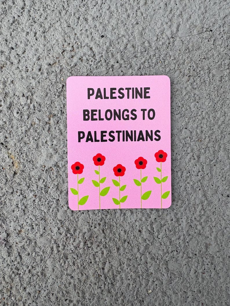 Może przedstawiać: R&oacute;żowy naklejka z tekstem "Palestine belongs to Palestinians" w czarnym kolorze. Pięć czerwonych kwiat&oacute;w z zielonymi łodygami i liśćmi znajduje się na dole naklejki.