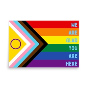 May include: A rainbow pride flag with a purple circle and a yellow background in the top left corner. The flag has the text "WE ARE GLAD YOU ARE HERE" in light blue letters on the right side.