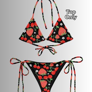 May include: A black bikini set featuring a repeating pattern of red strawberries, red cherries, and small white flowers. The triangle bikini top has adjustable neck and back ties, and the bikini bottom features side ties. The text Top Only is visible.