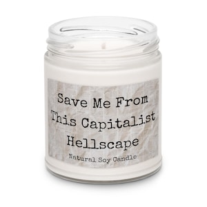 May include: A clear glass jar candle with a white wax interior. The label reads "Save Me From This Capitalist Hellscape" in black text. The bottom of the label says "Natural Soy Candle". The candle has a wick in the center.