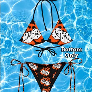 Può includere: Un bikini a due pezzi con un motivo a fiamme nero e arancione e grafiche di dadi bianchi. Il top presenta coppe triangolari con laccetti neri, mentre lo slip ha laccetti laterali. Il testo Bottom Only è stampato sul lato destro dell'immagine.