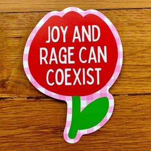 Peut inclure: Un autocollant en forme de fleur avec un centre rouge et une bordure vichy rose et blanche. Le texte blanc "JOY AND RAGE CAN COEXIST" est inscrit. La tige et la feuille sont vertes.