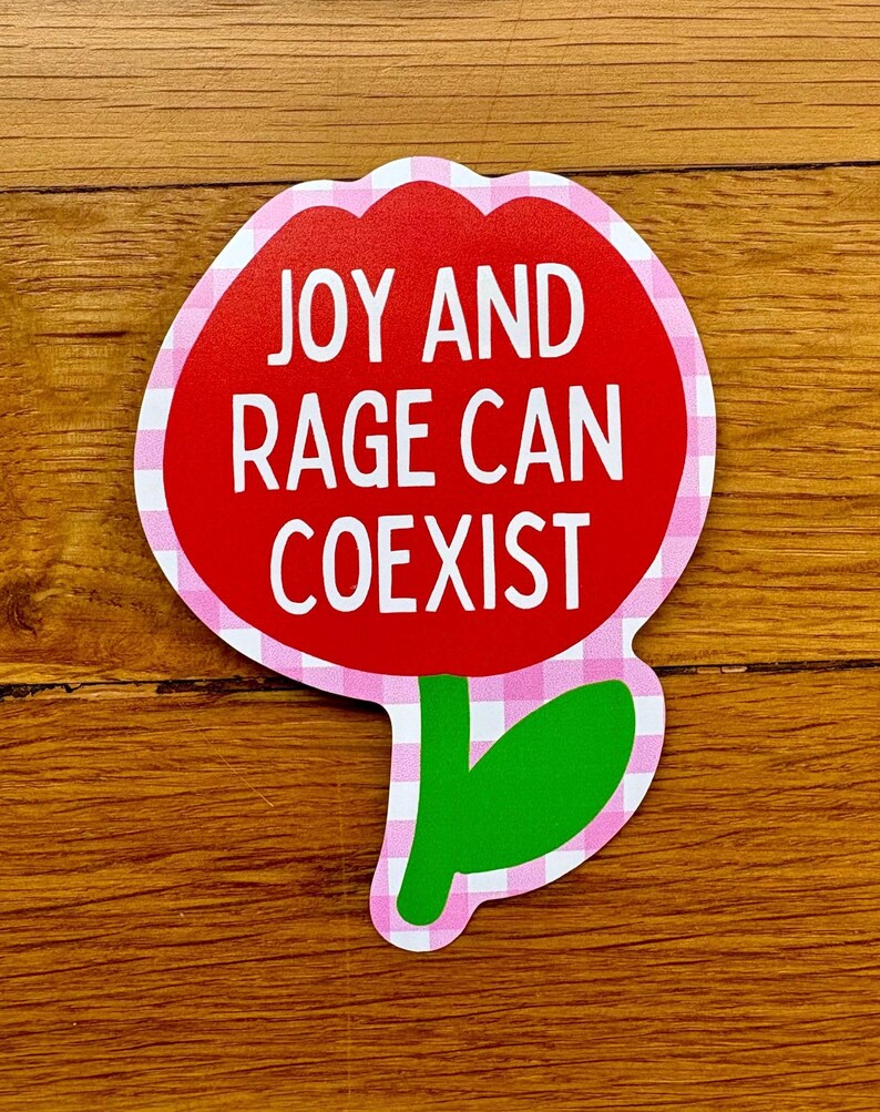 Peut inclure: Un autocollant en forme de fleur avec un centre rouge et une bordure vichy rose et blanche. Le texte blanc "JOY AND RAGE CAN COEXIST" est inscrit. La tige et la feuille sont vertes.