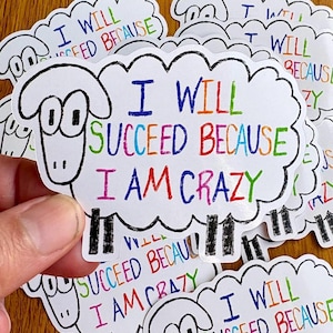 Può includere: Adesivi bianchi a forma di pecora con la scritta "I WILL SUCCEED BECAUSE I AM CRAZY" in lettere colorate. Gli adesivi hanno un contorno nero e sono su uno sfondo di legno.