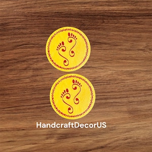 May include: Two yellow circular coasters with red decorative borders and red footprints in the center. The coasters are on a wood background.