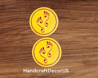 May include: Two yellow circular coasters with red decorative borders and red footprints in the center. The coasters are on a wood background.