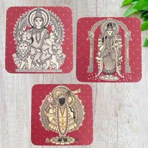 Pode incluir: Conjunto de tr&ecirc;s bases de copos quadradas com ilustra&ccedil;&otilde;es religiosas. Cada base apresenta uma divindade diferente em preto e branco, sobre um fundo vermelho com pequenas bolinhas douradas. As bases s&atilde;o provavelmente feitas de material absorvente.